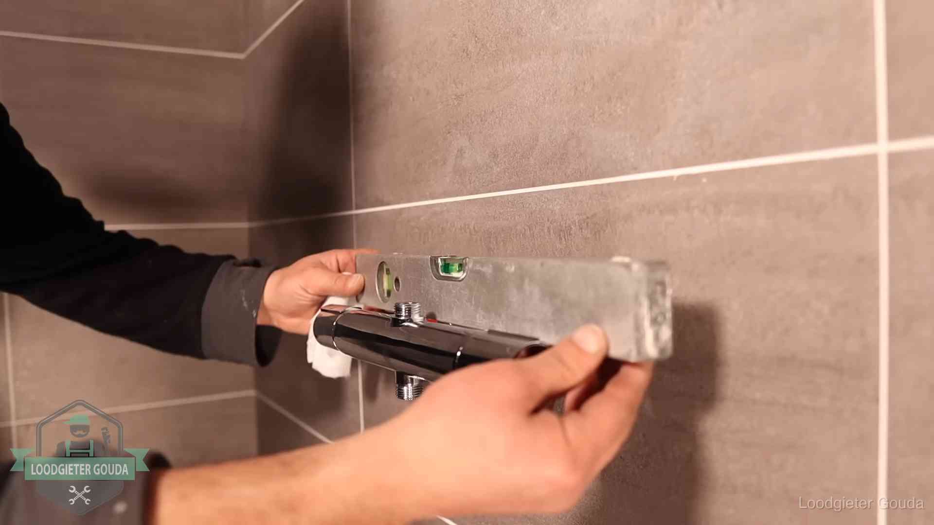 Loodgieter lijnt een douchekraan uit met een waterpas in een woning in Gouda