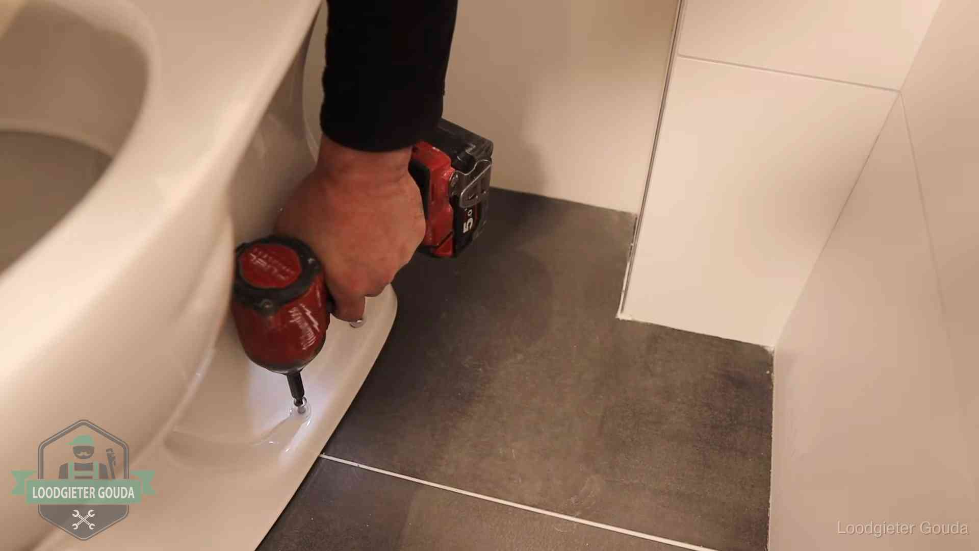Loodgieter zet de voet van een wc-pot vast op de tegelvloer in Gouda